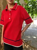 Buzo rojo de punto con cuello polo, botones blancos y mangas cortas con ribete blanco y azul marino.