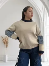 Sweater beige de tejido de punto con cuello redondo y puños en color azul marino. Mangas largas con parches de denim en los antebrazos.