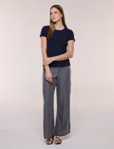 Remera básica de corte al cuerpo con textura acanalada, cuello redondo y mangas cortas. Presenta una pequeña placa metálica decorativa en el borde inferior.