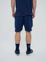 Bermuda deportiva Umbro de color azul marino, con inserciones laterales en color blanco y el logo de la marca estampado en la pierna izquierda.