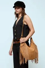 Cartera bandolera de gamuza sintética color marrón, con diseño de flecos largos en los laterales y base. Cuenta con correa ajustable y cierre en el compartimento principal.