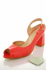 Sandalias de cuero charol color coral con taco mediano forrado, diseño open toe y tira ajustable en el talón. Presenta un aplique decorativo desmontable en forma de corazón blanco en la parte delantera.