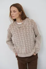 Buzo de tejido de punto con diseño reversible, cuello redondo y mangas largas. Presenta un patrón de trenzas en relieve con combinación de colores beige y marrón.
