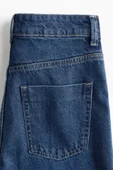 Jean de tiro alto con corte wide leg, confeccionado en denim rígido de lavado azul clásico. Presenta diseño de cinco bolsillos, cierre frontal con botón y ruedo desflecado.
