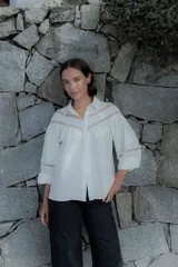 Camisa blanca de algodón con detalles de encaje y broderie en el pecho y mangas. Presenta cuello camisero, cierre frontal con botones y mangas tres cuartos con terminación elástica.