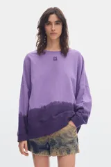 Buzo de felpa sin frisa color lila y morado con efecto degradé, cuello redondo, mangas largas y fit relajado. Incluye bordado pequeño en el centro del pecho.
