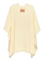 Ruana de lana color crema con bordes desflecados y etiqueta de cuero con logo de la marca en la parte superior.