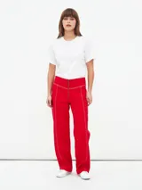 Pantalón de corte recto y tiro alto, color rojo, con costuras decorativas en contraste y cierre frontal con cremallera expuesta.