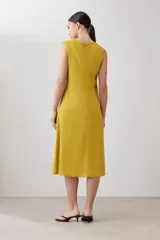 Vestido midi acampanado color mostaza, sin mangas, confeccionado en lino con detalle desflecado en los bordes. Incluye una bufanda del mismo material y color.