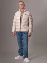 Campera acolchada color beige claro, con cuello alto y cierre frontal con cremallera. Tiene bolsillos laterales y logo de Calvin Klein en el pecho.