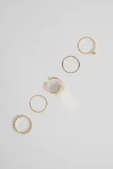 Pack de cinco anillos de metal dorado con diversos diseños, incluyendo uno con detalle de esfera, uno texturizado, uno liso y uno con diseño geométrico calado.