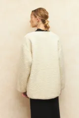 Abrigo gamulán de corderito color crudo, con alamares de cuero sintético negro y cierres metálicos.