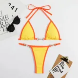 Bikini de dos piezas con corpiño triangular y bombacha colaless. El diseño destaca por sus detalles de cadenas doradas con perlas incrustadas en los breteles del corpiño y en los laterales de la bombacha. Presenta una combinación de colores vibrantes en amarillo y naranja.