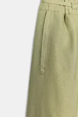 Pantalón ancho de tiro alto color beige claro, con cintura elástica, cordón ajustable y pinzas delanteras. Presenta bolsillos frontales y bolsillos de plastrón en la espalda. Incluye un cinturón del mismo tejido con apliques metálicos.