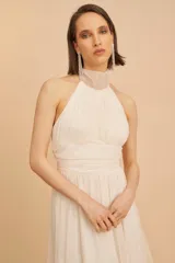 Vestido midi de fiesta color crudo, con cuello halter, cuerpo drapeado y falda de microtul plisado.