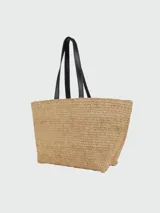 Tote bag de rafia natural con diseño tejido, asas largas de cuero negro y bordado frontal con el logo de la marca en hilo negro.