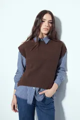Chaleco tejido sin mangas de color marrón, con cuello redondo y diseño de textura sutil. Presenta un corte recto con terminaciones acanaladas en el ruedo y hombros levemente estructurados.