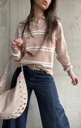Sweater de punto con rayas horizontales blancas y base en tono beige y rosado, cuello polo con botones y mangas largas.