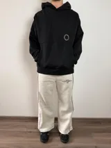 Pantalón tipo jogger de corte baggy, confeccionado en algodón color gris melange. Presenta una línea vertical negra a lo largo de la pierna y un estampado tipográfico pequeño en la parte superior frontal.