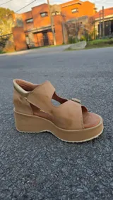 Sandalias de cuero color tostado con plataforma y taco chino, tiras frontales y laterales con hebillas ajustables y detalles en tono dorado texturizado.