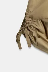 Pantalón culotte de tiro medio, color verde militar, con cintura elástica y bolsillos laterales ocultos. Presenta un diseño de bajo ancho con aberturas ajustables mediante cordones fruncidos en los laterales.