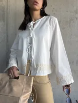 Chaqueta blanca de algodón con bordados florales en puños y ruedo, escote con lazos y mangas largas acampanadas.