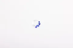 Anillo artesanal de vidrio transparente con diseño irregular y pequeñas esferas de vidrio en color azul profundo aplicadas en uno de sus lados.