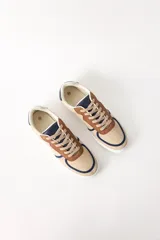Zapatillas urbanas color beige con detalles en marrón y azul marino, cordones marrones y suela blanca.