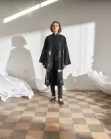 Capa negra de paño de lana con cuello mao y cierre frontal con ganchos ocultos. Estampado serigráfico negro brillante en cuerpo y cuello.