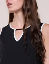 Blusa sin mangas de seda fría marca Rio & Rian, color blanco con ribetes negros en cuello y sisas. Presenta un escote redondo con abertura tipo gota en el frente y un aplique metálico decorativo.