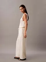 Pantalón de pierna ancha color beige, confeccionado en lino y algodón. Presenta cintura elástica con cordón ajustable, dos bolsillos laterales y un bolsillo trasero.