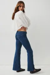 Jeans de denim azul de tiro bajo con leve elasticidad. Presentan un corte ajustado hasta el muslo y acampanado desde la rodilla. El cierre es frontal con botones en una pretina prolongada y cuenta con bolsillos delanteros de parche y bolsillos traseros.