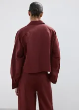 Camisa oversize color borravino, de manga larga con puños abotonados, cuello camisero, dos bolsillos de parche en el frente y cierre delantero con botones.