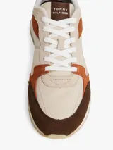 Zapatillas Tommy Hilfiger de estilo retro con paneles de ante y tela en tonos beige, marrón y naranja. Presentan suela gruesa dentada de goma, cierre con cordones y detalles de la marca en la lengüeta y el talón.