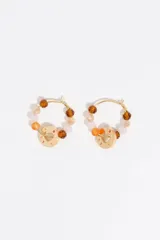 Caravanas de aro con acabado metálico dorado, decoradas con cristales facetados en tonos marrón, beige, rosado y naranja. Incluyen un dije circular con calado de corazón y logo grabado.