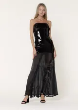 Vestido largo de fiesta con escote strapless. La parte superior presenta un diseño ajustado cubierto de lentejuelas negras, mientras que la parte inferior está confeccionada en chiffon plisado con paneles godet que aportan volumen y movimiento.