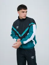 Campera deportiva Umbro modelo Beat, confeccionada en nylon ligero con diseño de bloques de color en blanco, azul marino y verde azulado. Presenta cierre frontal, cuello alto y elásticos en puños y cintura.