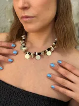 Collar corto con cuentas irregulares de piedra en tonos tierra y blanco, nácar y dijes metálicos redondos (algunos dorados y otros plateados).