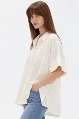 Camisa de viscosa color natural, de corte holgado, con cuello camisero, mangas cortas y cierre frontal con botones.