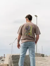 Remera Brixton oversize de algodón, color marrón con efecto acid wash, manga corta y estampa en la espalda de flores de mburucuyá con el texto vertical en color verde.