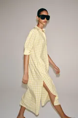 Vestido midi camisero de algodón, color amarillo con estampado a cuadros. Cuenta con cuello solapa, escote en V, mangas cortas con puño y bolsillos laterales ocultos en la costura, con diseño evasé.