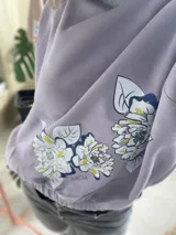 Buzo de algodón color tostado, de corte cropped y estilo oversize. Presenta cuello redondo, mangas largas con puños ajustados y elástico en la cintura. Destaca por una estampa exclusiva de flores en el frente y en una de las mangas.