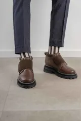 Botinetas de caña baja con suela track gruesa, combinando cuero negro en la puntera, gamuza marrón en el lateral y detalles de textura animal print tipo serpiente en tonos marrones. Presenta un cierre de solapa con velcro en el empeine.