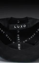 Gorra de béisbol negra, estilo clásico de seis paneles, con visera curva y botón superior. Presenta un tejido de sarga liso.