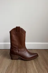 Bota estilo western de caña media, confeccionada en cuero color marrón, con taco cuadrado y punta ligeramente afinada.