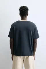 Camiseta de manga corta y cuello redondo, color azul marino, con ribete de contraste en color crema alrededor del cuello.