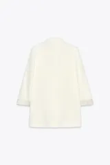 Blazer blanco de lino con cuello solapa, manga larga con hombreras y puños con vuelta estampada. Tiene bolsillos delanteros con solapa y cierre frontal con botón.