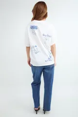 Camiseta de corte oversize, color blanco, con cuello redondo, mangas cortas y estampa botánica pequeña en el pecho.