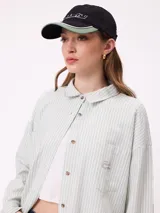 Gorra con visera de estilo urbano, color negro con detalles en verde en la parte inferior de la visera y bordado frontal con el logo de la marca.