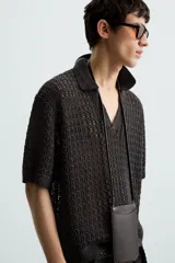 Polo de manga corta confeccionado en tejido de punto calado con estructura abierta. Presenta un diseño de corte relajado, cuello solapa con abertura frontal en pico y terminaciones acanaladas en puños y bajo.